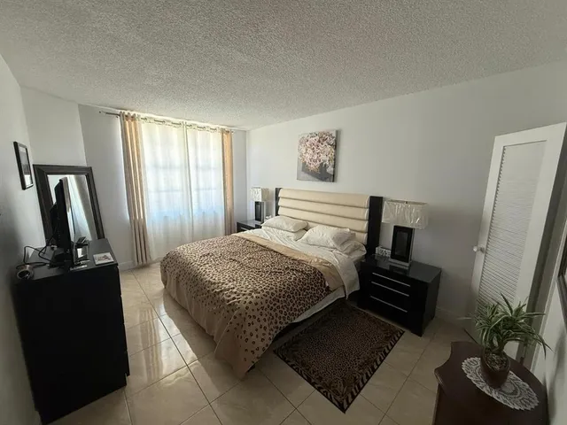 a bedroom with a bed table flat screen tv and a window