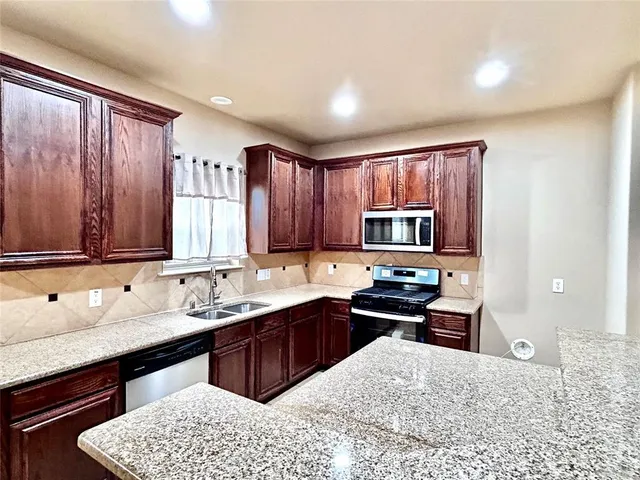 a kitchen with stainless steel appliances granite countertop a sink dishwasher stove and cabinets with wooden floor
