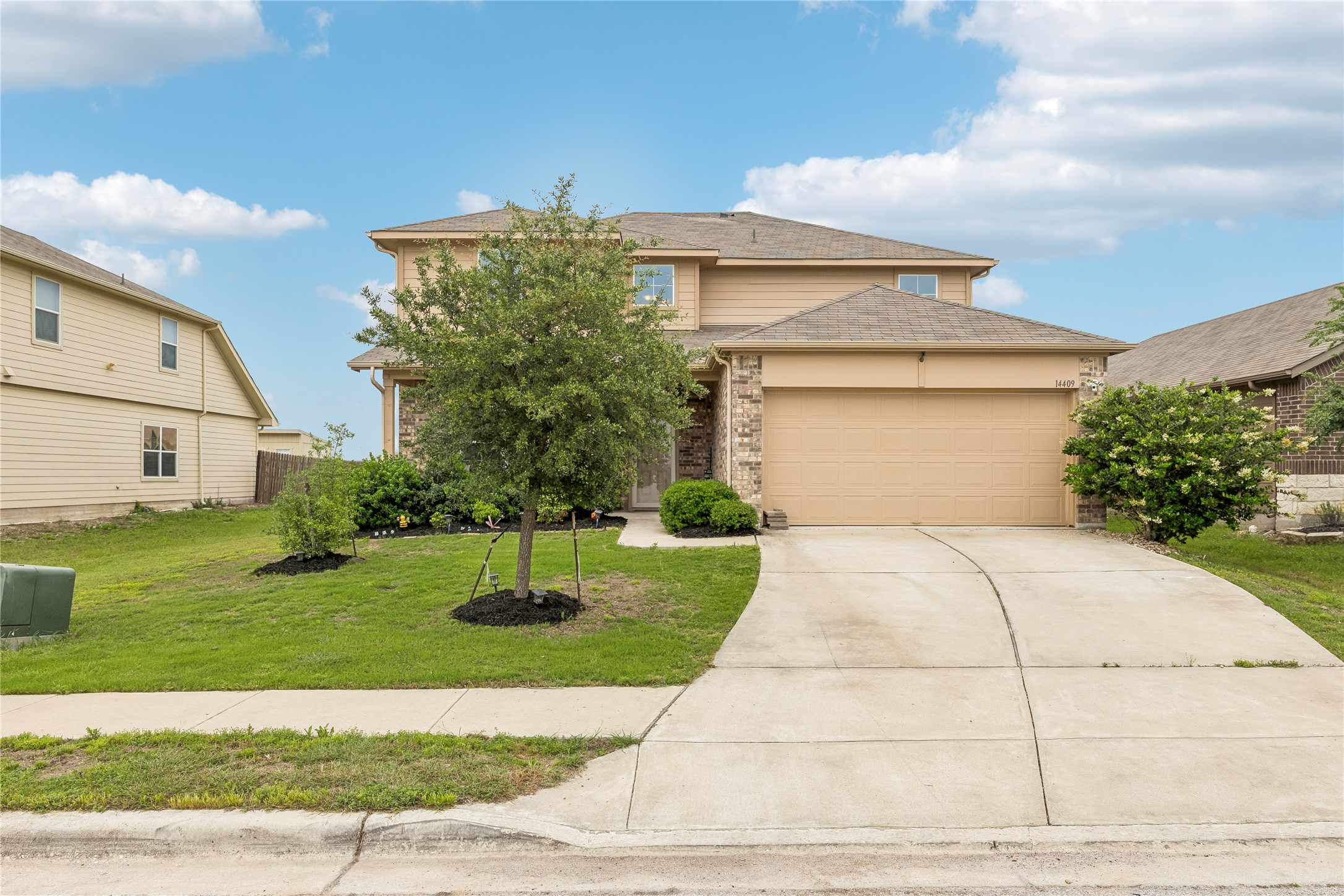 14409 Estuary Road Manor, TX 78653 - Photo 3 of 24 Two-story residence featuring a two-car garage, stone accents, tan siding, a concrete driveway, and a manicured lawn with mature landscaping