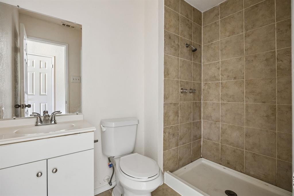 6221 Pine Street Rowlett, TX 75089 - Photo 7 of 12 Bathroom featuring a vanity with an integrated sink, a commode, a walk-in shower with tile surround, and a wall-mounted mirror