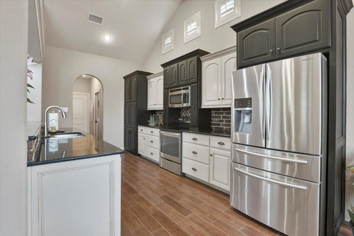 1125 17th Street Shallowater, TX 79363 - Photo 11 of 32 a kitchen with stainless steel appliances granite countertop a refrigerator a stove and a sink with wooden floor