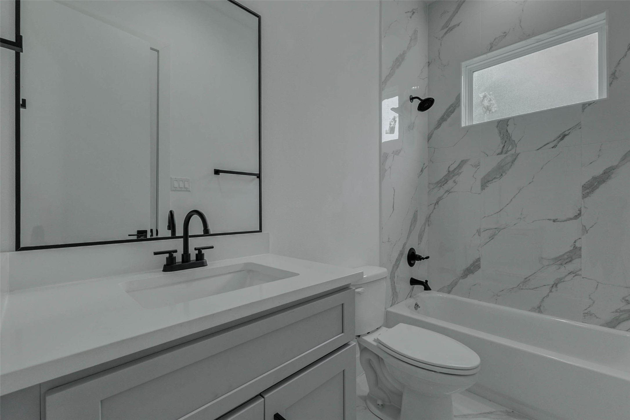 5705 Elysium Street Houston, TX 77091 - Photo 7 of 22 A stylish bathroom view highlights modern tile-look finishes, a glass shower enclosure, and black hardware, giving the space a crisp, elevated feel.