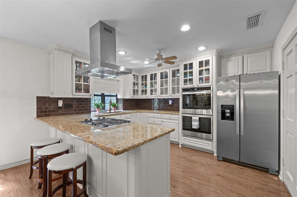 318 Ridge Creek Road Waxahachie, TX 75167 - Photo 13 of 40 Kitchen featuring white cabinetry, stainless steel appliances, granite-finish countertops, tile backsplash, and wood-finish flooring