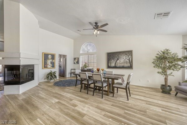 1536 Pony Ranch Circle Henderson, NV 89014 - Photo 4 of 24 Dining space featuring a ceiling fan, light wood-type flooring, a multi sided fireplace, and high vaulted ceiling