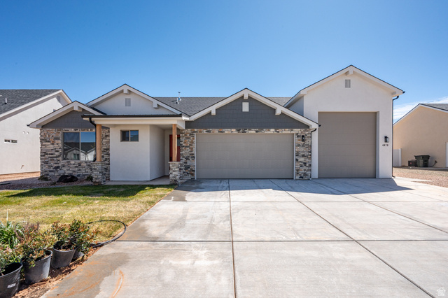 View of front of property featuring a garage, driveway, stone siding, and stucco siding