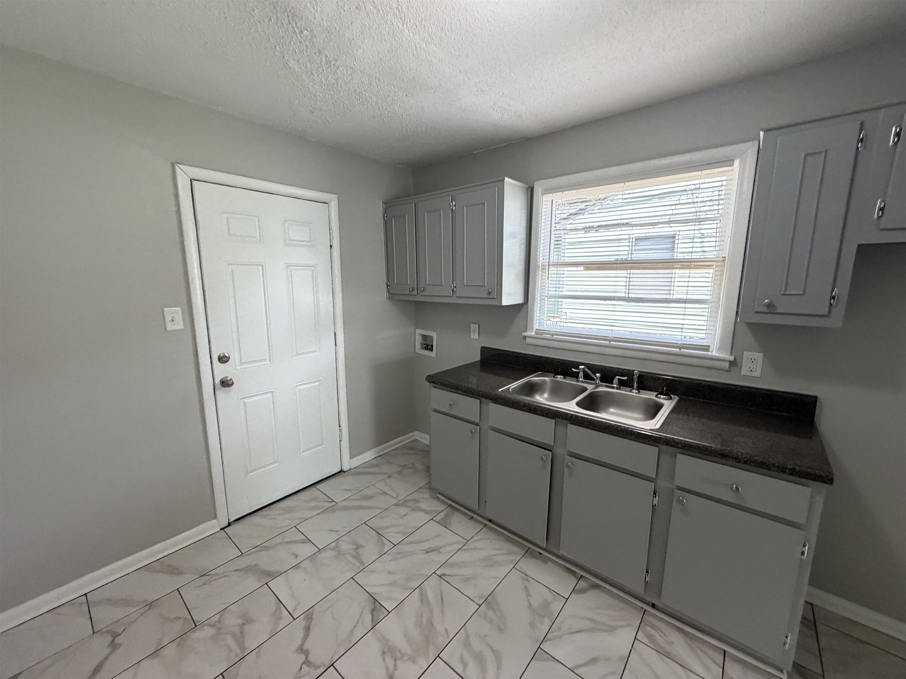 3525 Rochester Road Memphis, TN 38109 - Photo 8 of 10 Kitchen area featuring gray cabinetry, dark countertops, a double-basin stainless steel sink, and light-toned tile flooring