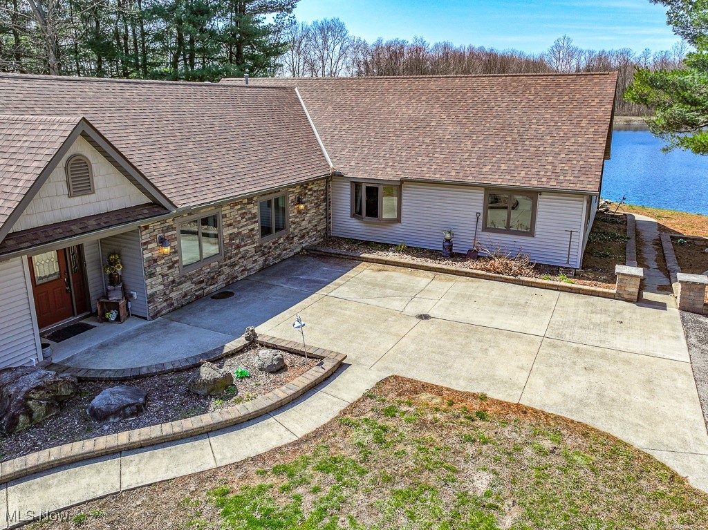 Rear view of property with stone siding, a shingled roof, a water view, and a patio area