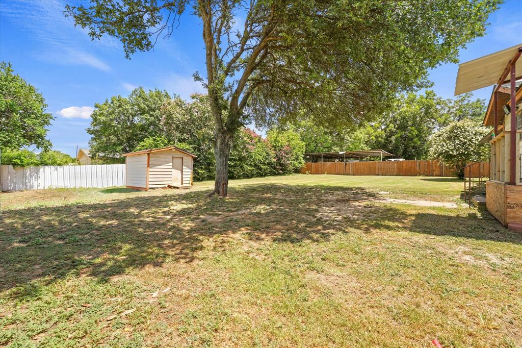 1100 North Church Street Decatur, TX 76234 - Photo 14 of 14 Expansive backyard featuring a mature tree, a white storage shed, and a combination of wood and white privacy fencing