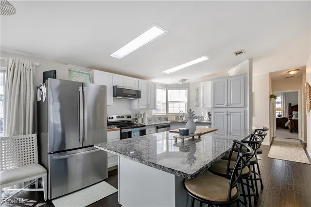 a kitchen with stainless steel appliances granite countertop a dining table chairs refrigerator and sink