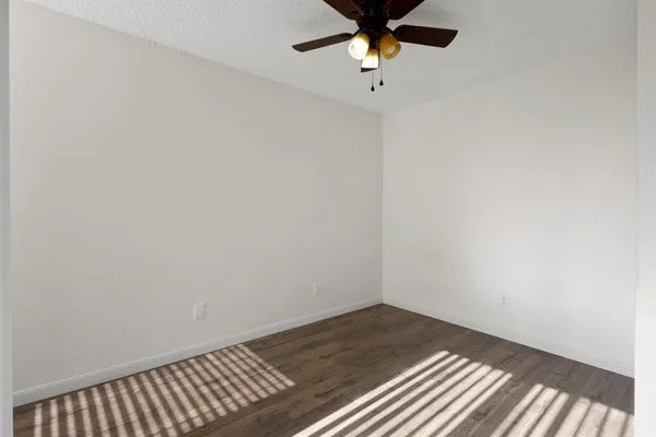 an empty room with a chandelier fan and wooden floor