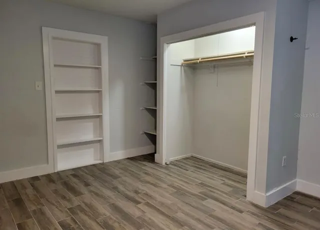 a view of an empty room with wooden floor and closet