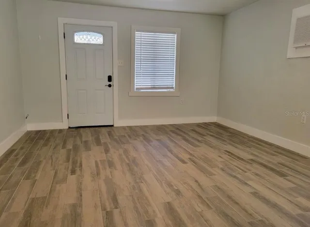 a view of an empty room with wooden floor and a window