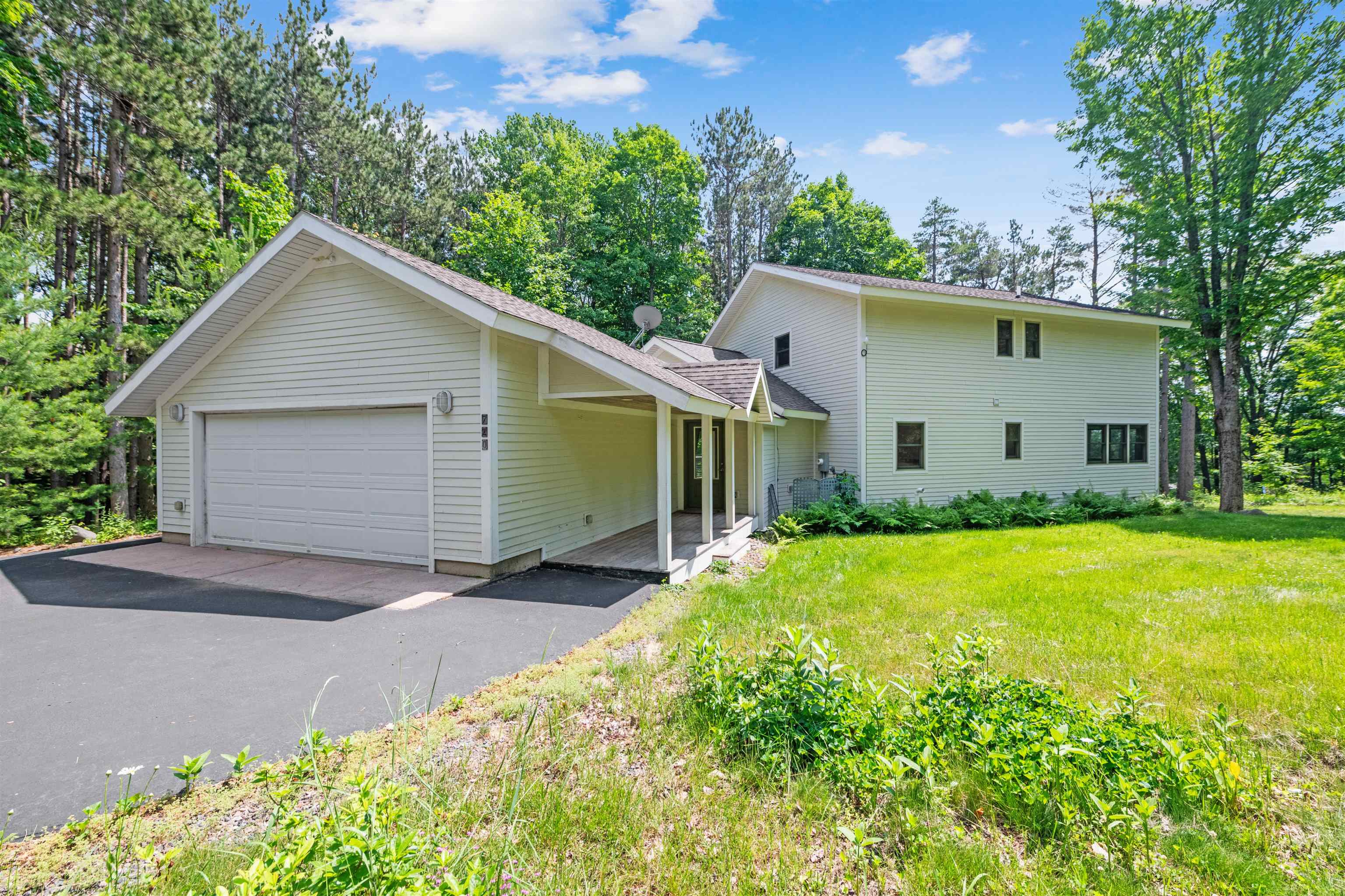 720 Rice Avenue Bayfield, WI 54814 - Photo 3 of 47 View of property exterior with an attached garage, a lawn, a shingled roof, and view of wooded area