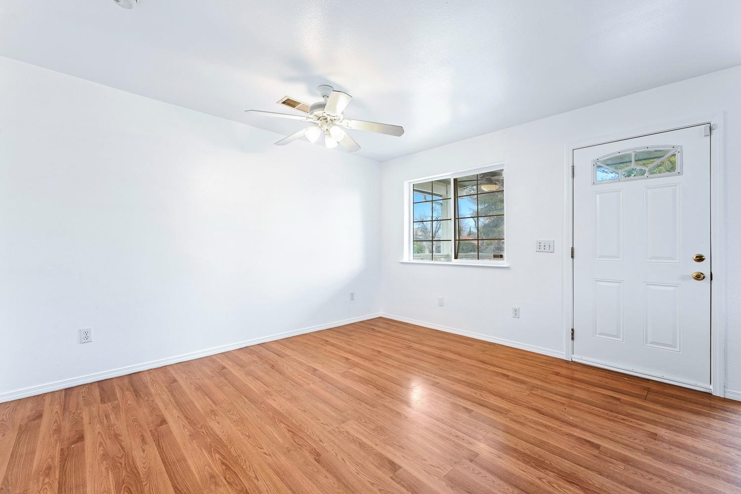 249 Jackson Street Coalinga, CA 93210 - Photo 6 of 42 an empty room with wooden floor chandelier fan and windows