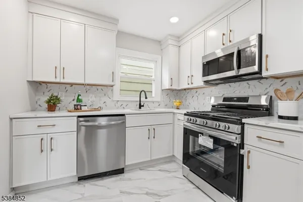 a kitchen with stainless steel appliances granite countertop white cabinets a stove a sink and a microwave