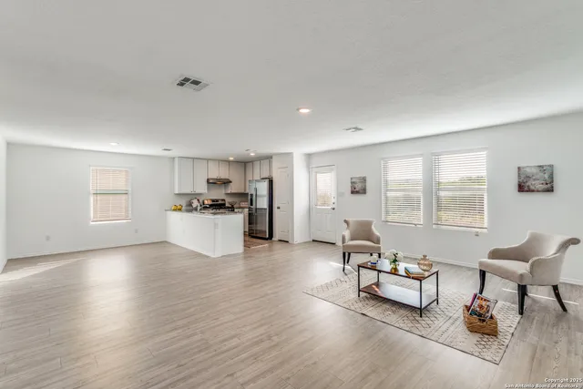 a living room with furniture and kitchen area with wooden floor