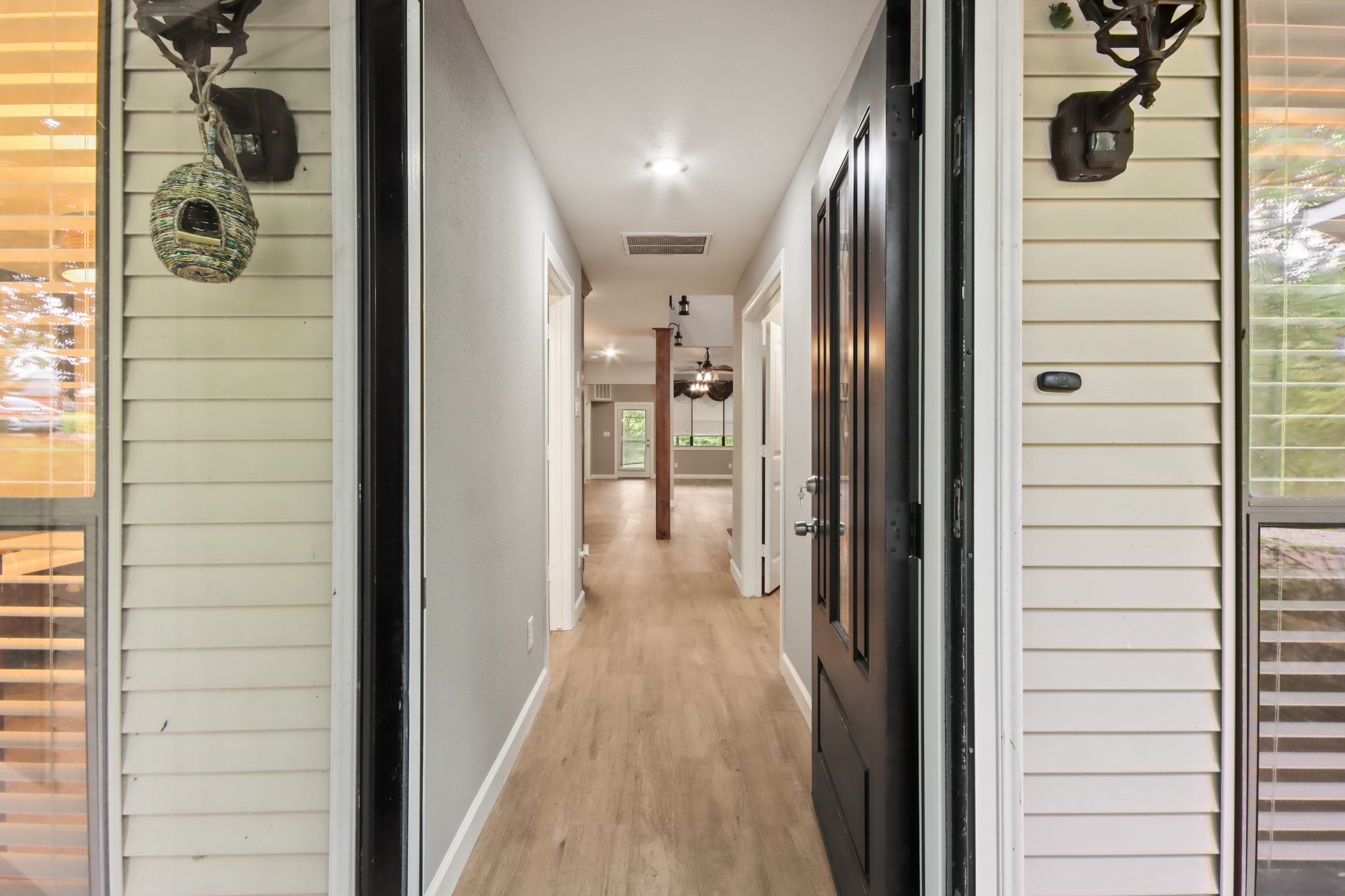 35 Susan Drive Cleveland, TX 77327 - Photo 3 of 33 This photo shows the entrance of a home featuring a welcoming hallway with light wood flooring and neutral walls. The space is well-lit, leading to an open area with large windows at the far end, offering a view of greenery outside.