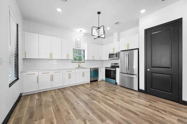 a large kitchen with stainless steel appliances kitchen island granite countertop a refrigerator a stove a sink dishwasher and white cabinets with wooden floor