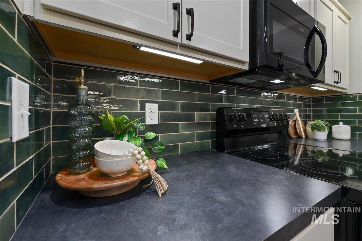 12781 Ashfield Street Caldwell, ID 83607 - Photo 12 of 36 Kitchen with dark countertops, white cabinetry, black appliances, dark wood-style floors, and an island with sink