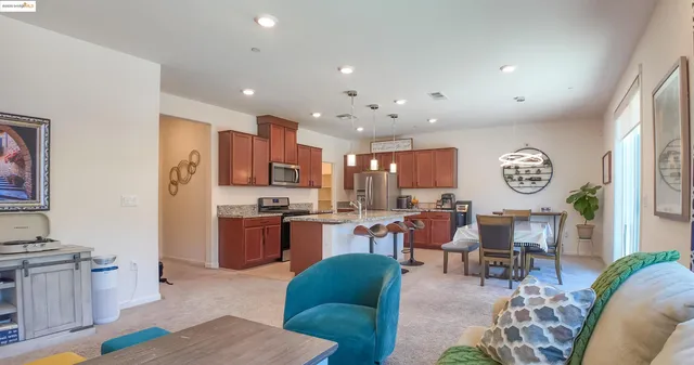 a living room with stainless steel appliances furniture a rug and a kitchen