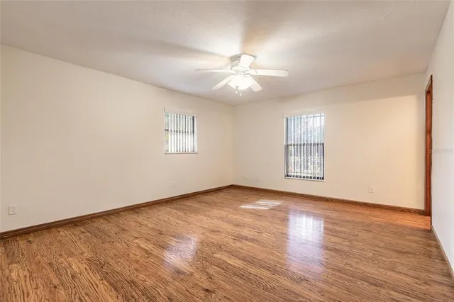 an empty room with wooden floor chandelier fan and windows