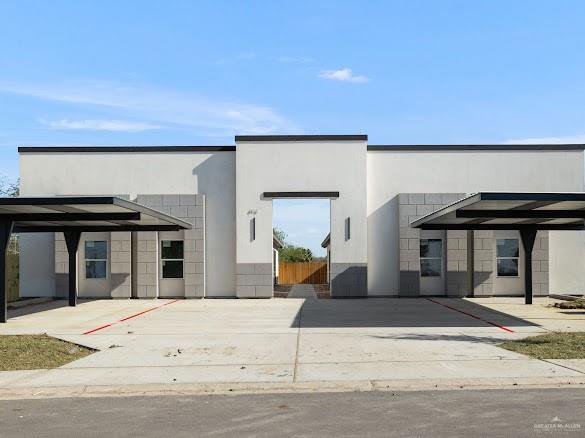 Modern facade featuring a central arched entryway, two carport structures, and a combination of smooth stucco and block finishes