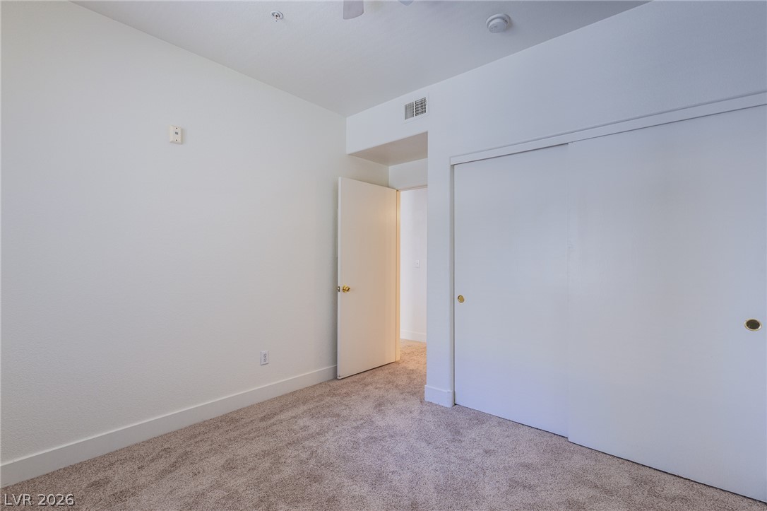 9050 West Warm Springs Road, Unit 1011 Las Vegas, NV 89148 - Photo 11 of 32 A spacious, neutral-toned room features soft carpeting and convenient sliding closet doors.