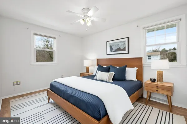 a bedroom with a bed and a lamp on dresser with wooden floor
