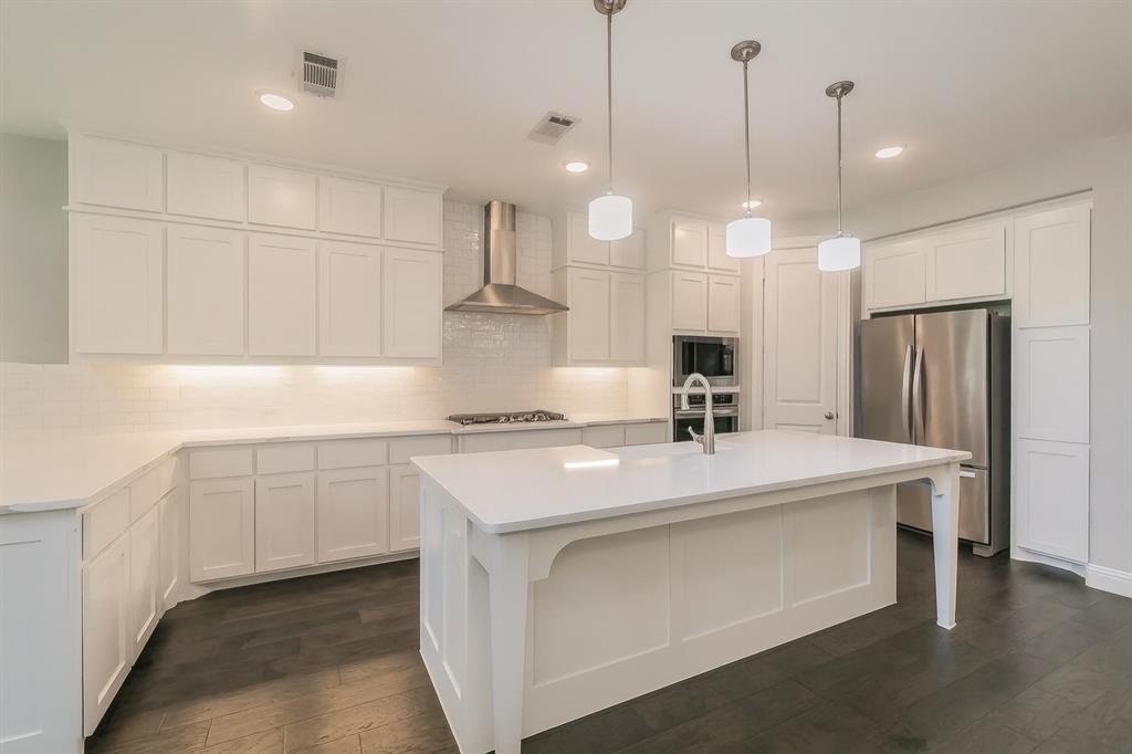 1908 Grey Bark Street Fort Worth, TX 76008 - Photo 6 of 31 Kitchen featuring appliances with stainless steel finishes, a kitchen island with sink, wall chimney exhaust hood, white cabinetry, and a kitchen bar