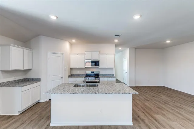 a kitchen with kitchen island a stove a sink a refrigerator and white cabinets with wooden floor