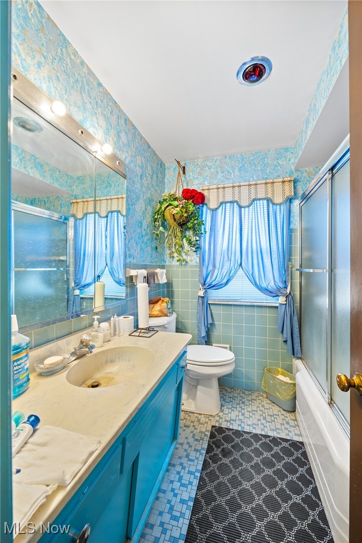 920 Clinton Avenue Cleveland, OH 44121 - Photo 11 of 14 Full bathroom featuring toilet, tile patterned flooring, vanity, bath / shower combo with glass door, and tile walls