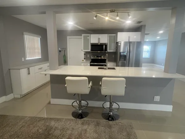 a kitchen with stainless steel appliances kitchen island granite countertop a table chairs refrigerator and microwave