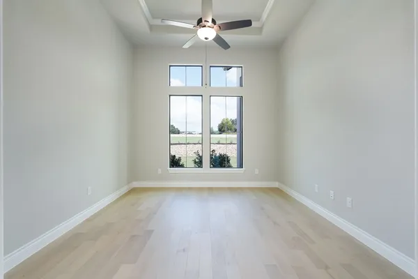 an empty room with wooden floor chandelier fan and windows