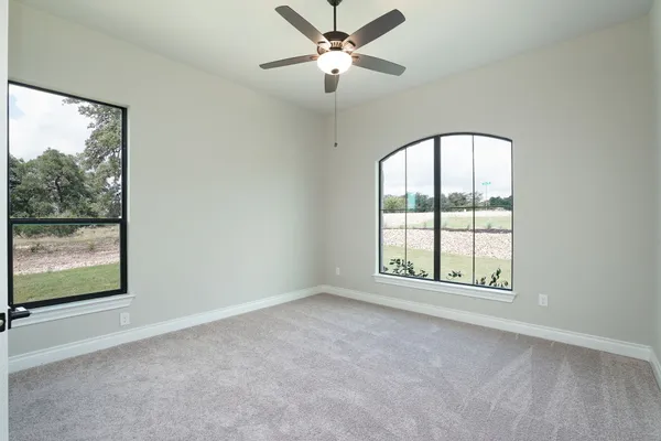 an empty room with chandelier fan and windows