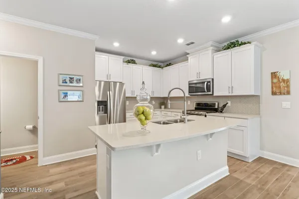 a kitchen with stainless steel appliances a stove a sink a refrigerator white cabinets and chairs