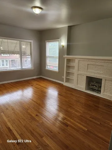 an empty room with wooden floor fireplace and windows