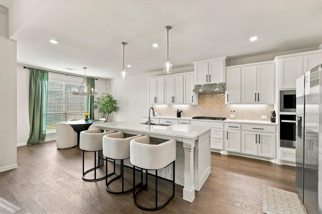 137 Chisos Court Rhome, TX 76078 - Photo 19 of 40 Kitchen featuring a large island with a countertop, shaker cabinetry, stainless steel appliances, a tile backsplash, and wood-finish flooring