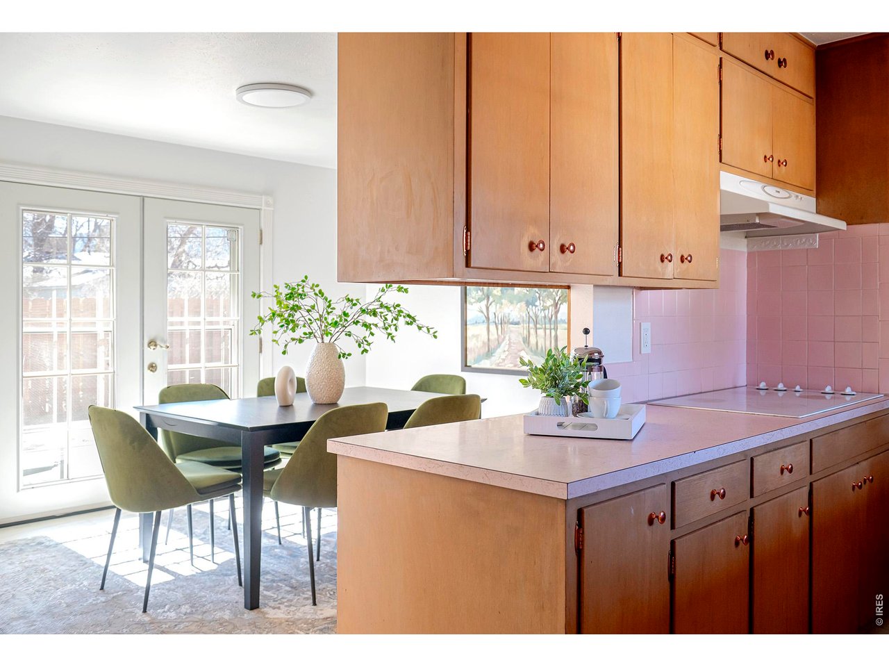 2410 Grape Avenue Boulder, CO 80304 - Photo 12 of 50 Warm wood cabinetry and clean, horizontal lines anchor the kitchen in authentic mid-century style, while soft pink countertops add a nostalgic pop of vintage charm. The open sightline to the dining area and French doors beyond