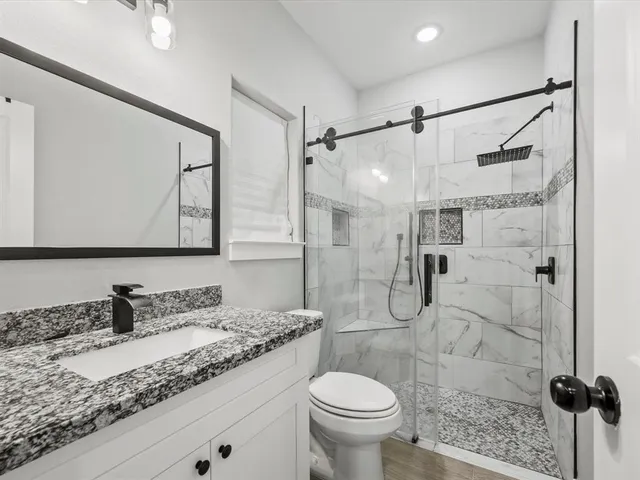 a bathroom with a granite countertop sink a toilet and shower