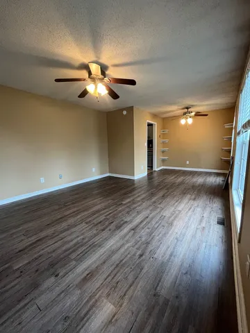 a view of an empty room with wooden floor and a ceiling fan