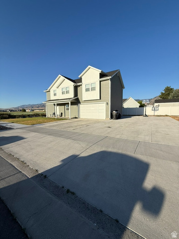1886 North 300 West Logan, UT 84341 - Photo 3 of 18 Two-story residence featuring light gray siding with white vertical accents, a dark shingle roof, an attached two-car garage, and a covered front porch