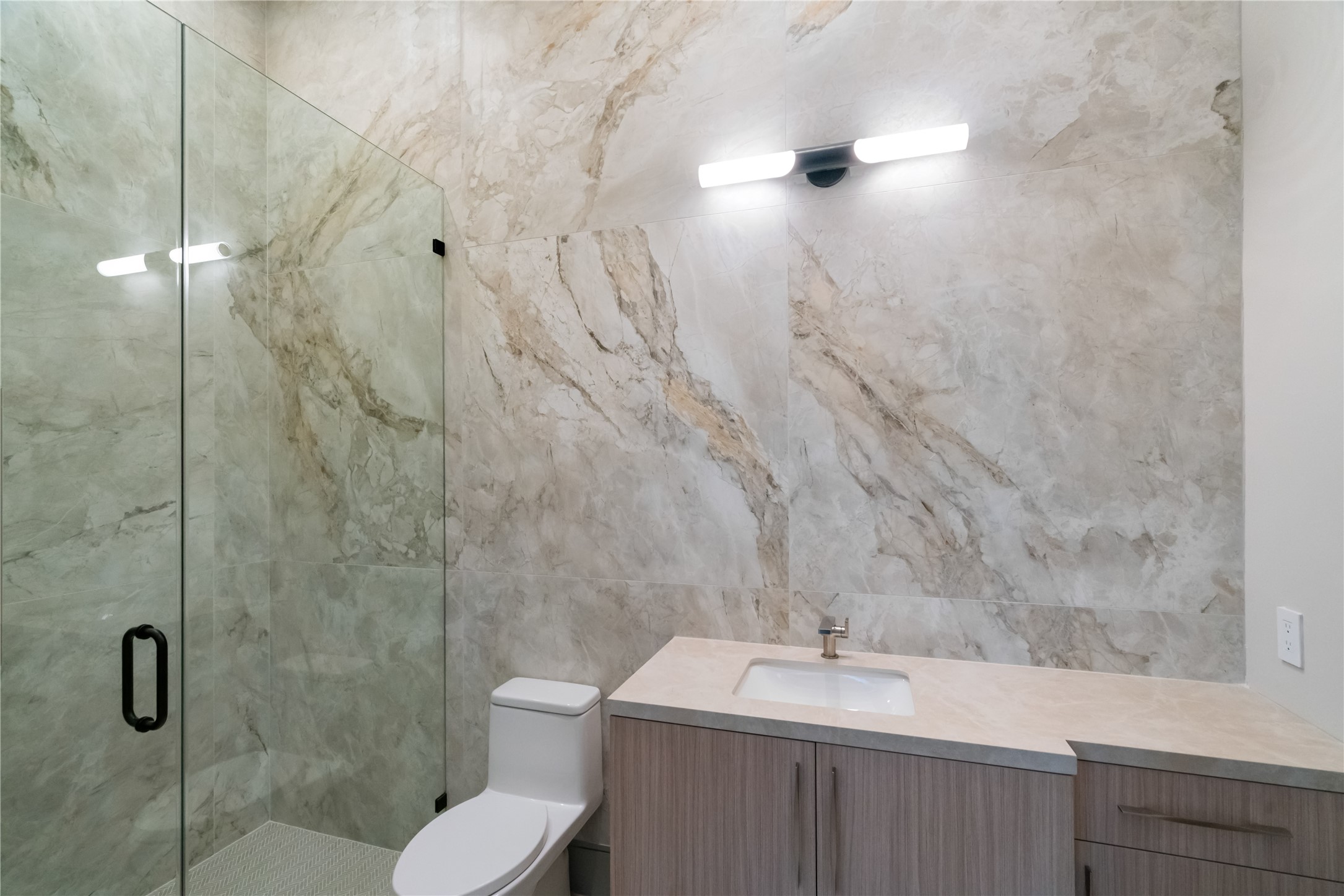 47 Pronghorn Place Spring, TX 77389 - Photo 23 of 44 This modern bathroom features elegant marble-like wall tiles, a sleek glass-enclosed shower, and a stylish vanity with ample storage. The lighting is contemporary and enhances the room's clean, sophisticated look.