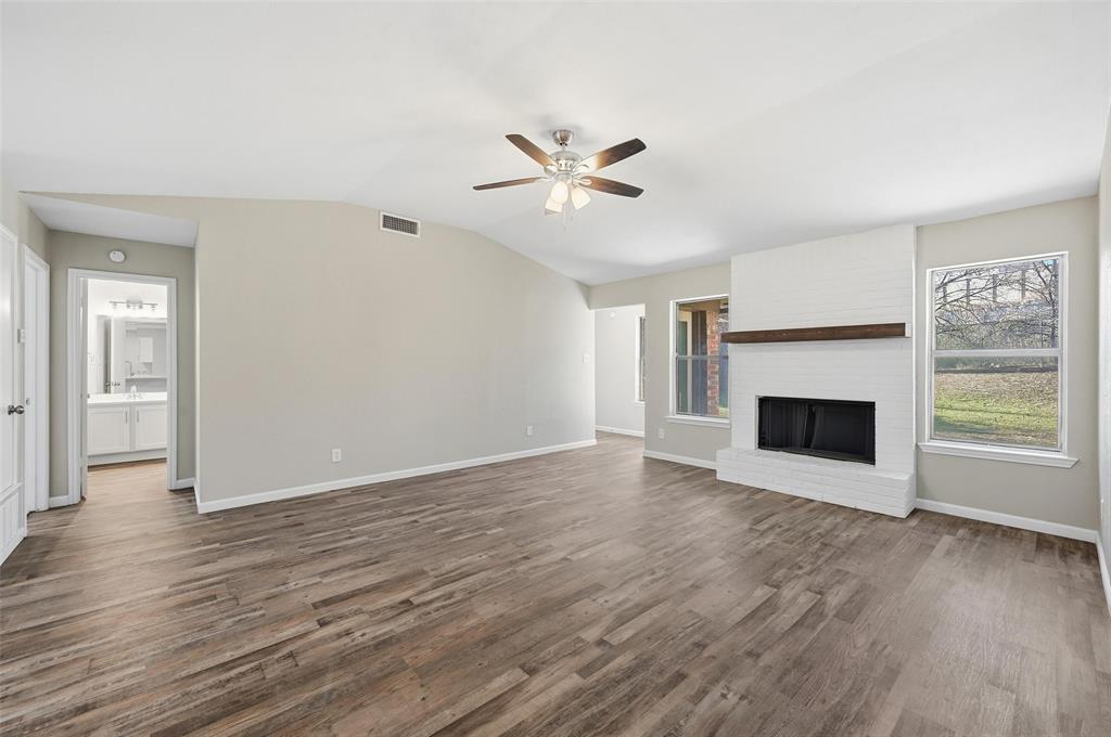 705 Timberoaks Drive Azle, TX 76020 - Photo 8 of 27 an empty room with wooden floor a fireplace a ceiling fan and windows