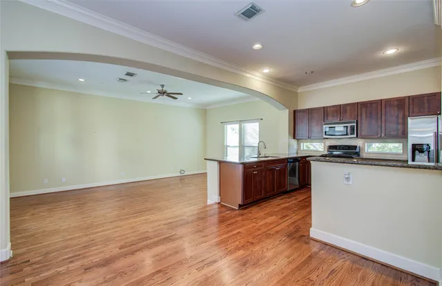 a large kitchen with stainless steel appliances granite countertop a stove a sink a refrigerator white cabinets and wooden floor