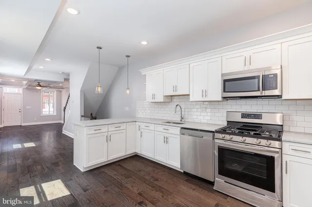 a kitchen with stainless steel appliances white cabinets a sink a stove a microwave and wooden floors