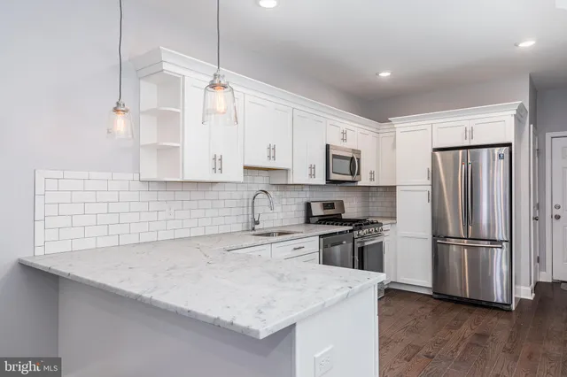 a kitchen with granite countertop a refrigerator a sink dishwasher a stove and white cabinets with wooden floor