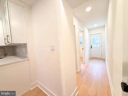 a view of a hallway to an empty room with wooden floor and a window