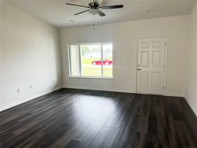 an empty room with wooden floor ceiling fan and windows