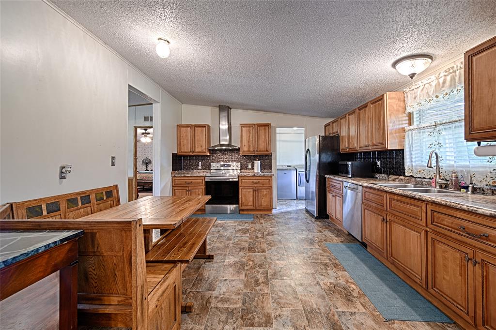 1670 Smith Circle Combine, TX 75159 - Photo 6 of 31 Kitchen with brown cabinetry, tasteful backsplash, stainless steel appliances, stone finish floors, and a textured ceiling