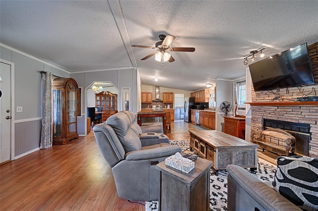 1670 Smith Circle Combine, TX 75159 - Photo 9 of 31 Living area with a textured ceiling, a stone fireplace, crown molding, light wood-style floors, and ceiling fan
